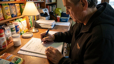 A person writing a short entry on a cleaning log sheet at closing time